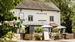 A white building with a sign reading "VILLAGE PUB" and a signboard displaying opening times. - The Bell Inn (Ladbroke)