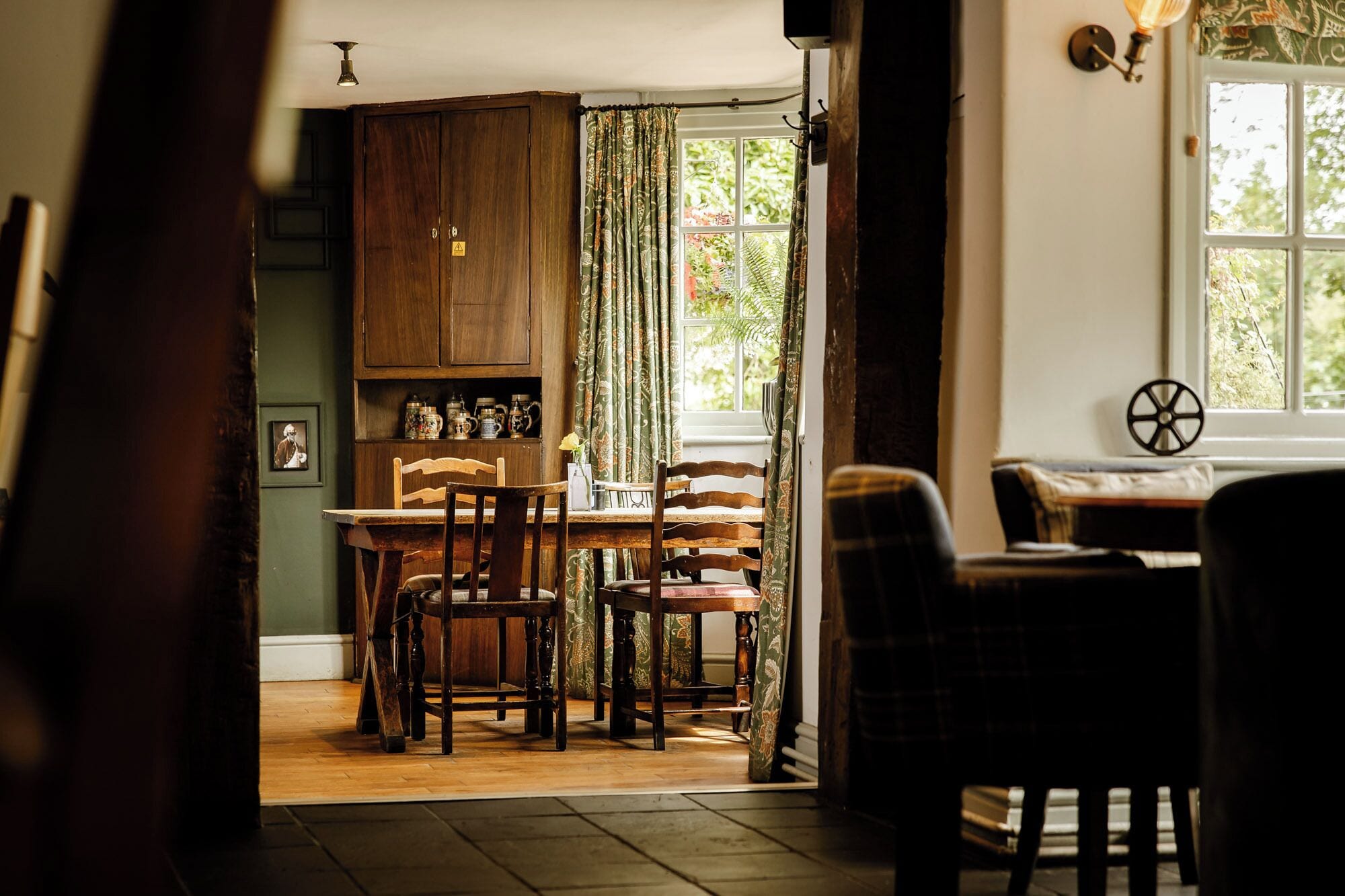 A cozy dining area with wooden furniture, a window with a view of greenery, and a traditional kitchen with wooden cabinets.