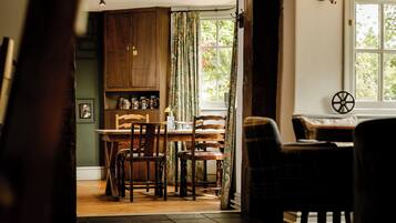 A cozy dining area with wooden furniture, a window with a view of greenery, and a traditional kitchen with wooden cabinets.