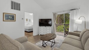 A living room with a TV, sofa, and a view of a bedroom and balcony. - Seagrove 2BR near Lake & Beach + Free Tickets: Bikes, Dolphin Cruise & More! (Santa Rosa Beach)