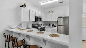 A modern kitchen with white cabinetry, stainless steel appliances, and a long countertop with decorative coasters. - Seagrove 2BR near Lake & Beach + Free Tickets: Bikes, Dolphin Cruise & More! (Santa Rosa Beach)