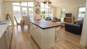 A spacious kitchen with a large island, wooden flooring, and a dining area with chairs and a table. - Kingfisher Lodge (Skipton)
