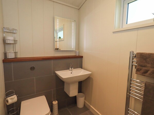 A bathroom with a white sink, a mirror with lights, a toilet, and a towel rack. - Kingfisher Lodge (Skipton)