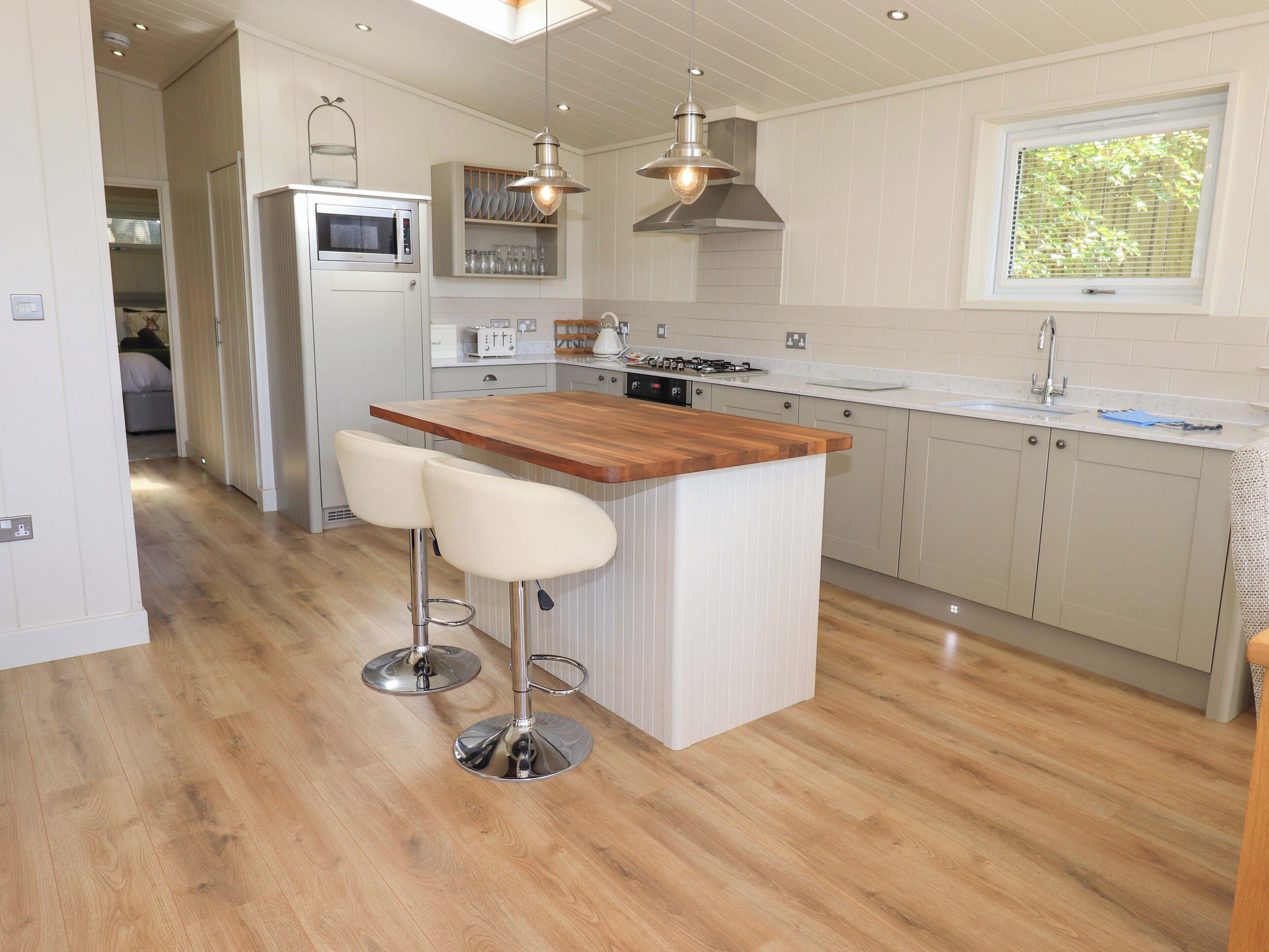 A modern kitchen with a wooden island, bar stools, stainless steel appliances, and pendant lighting.
