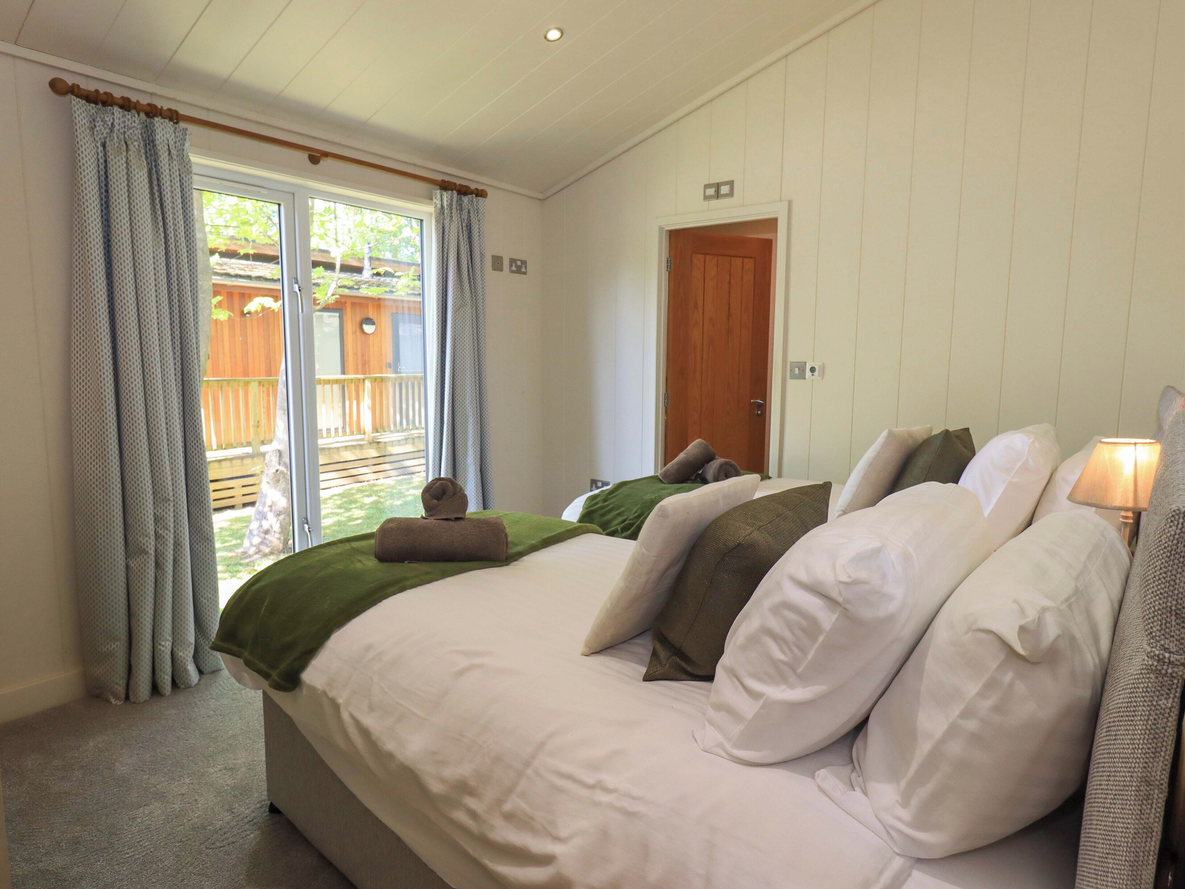 A bedroom with a bed, pillows, a bedside lamp, a window with curtains, and a door.