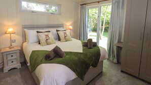 A bedroom with a bed, two bedside lamps, a window, and a wardrobe. - Kingfisher Lodge (Skipton)