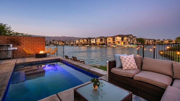An outdoor pool area with a grill, lounge chairs, and a view of a residential area across a body of water. - Solmar at Terra Lago Private Lake House With Free Pool Heating for any 3nights stay (Indio)