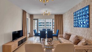 A modern living room with a TV, sofa, and dining area. - Bellavista - Elegant -2BR -Fountain View (Dubai)