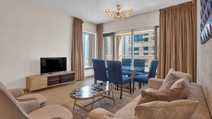 A modern living room with a TV, comfortable seating, a dining area, and large windows with curtains. - Bellavista - Elegant -2BR -Fountain View (Dubai)