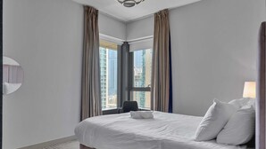 A hotel room with a large bed, a chair, a window with curtains, and a view of tall buildings. - Bellavista - Elegant -2BR -Fountain View (Dubai)