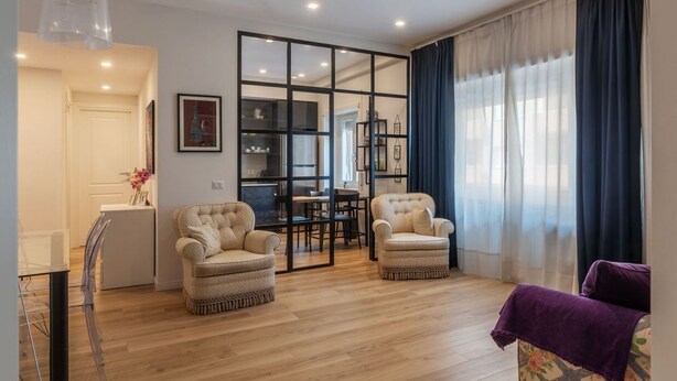 Un salon moderne avec deux fauteuils, un coin repas et une cuisine en arrière-plan.