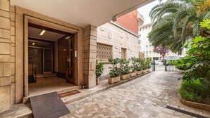 Une cour dallée de pierres, avec une entrée en bois, des plantes en pot et un palmier.