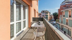 Ein Balkon mit Tisch und Stühlen und Blick auf die Straße, sowie ein mehrstöckiges Gebäude.