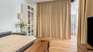 Ein modernes Schlafzimmer mit einem Bett, einem Nachttisch aus Holz, einem Bücherregal, einer Topfpflanze und einer Glastür zum Balkon.