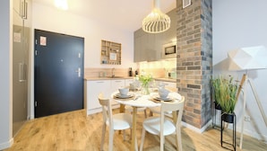 A modern kitchen with a dining area, featuring a round table set for four, a black door, and a brick accent wall. - Apartamenty Sun & Snow Koło Brzegu SPA (Kolobrzeg)