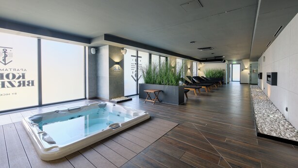 A modern spa area with a large hot tub, lounge chairs, and a wall with a sign. - Apartamenty Sun & Snow Koło Brzegu SPA (Kolobrzeg)