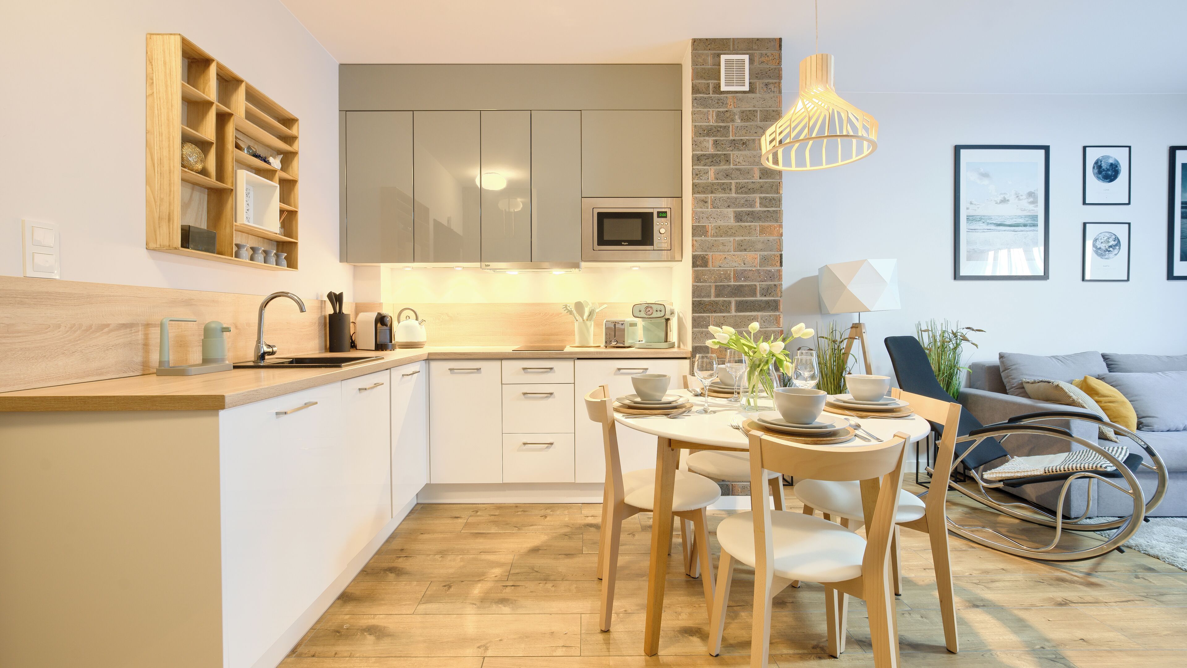 Una cucina moderna con mobili bianchi, un piano di lavoro in legno e un'area pranzo con tavolo imbandito per quattro persone.