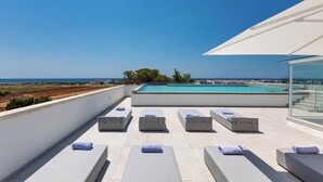 Une terrasse sur le toit avec des chaises longues, une piscine et une vue dégagée sur la mer.