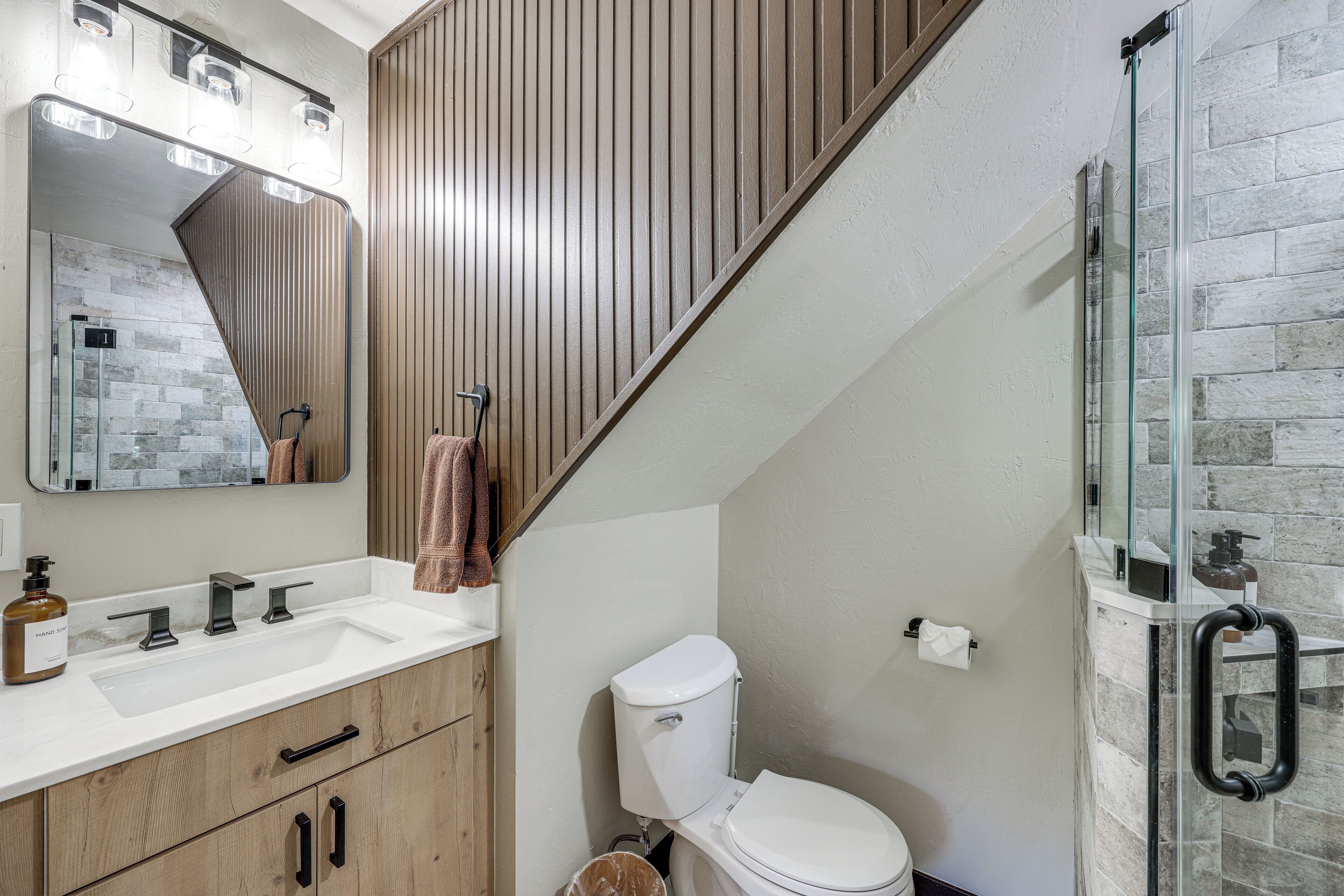 A bathroom with a wooden vanity, a white sink, a toilet, and a glass shower enclosure.