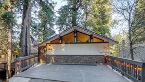 A lodge with a wooden deck, stone wall, and a flag. - Modern Lake Arrowhead Retreat: 3 Mi to Village (Lake Arrowhead)