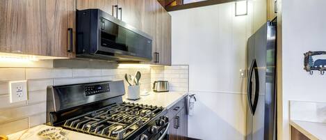 Una cocina moderna con estufa a gas, microondas y refrigerador de acero inoxidable.