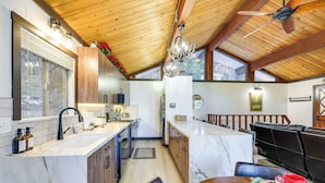 A modern kitchen with wooden cabinets, a marble countertop, and a dining area with a table set for two. - Modern Lake Arrowhead Retreat: 3 Mi to Village (Lake Arrowhead)