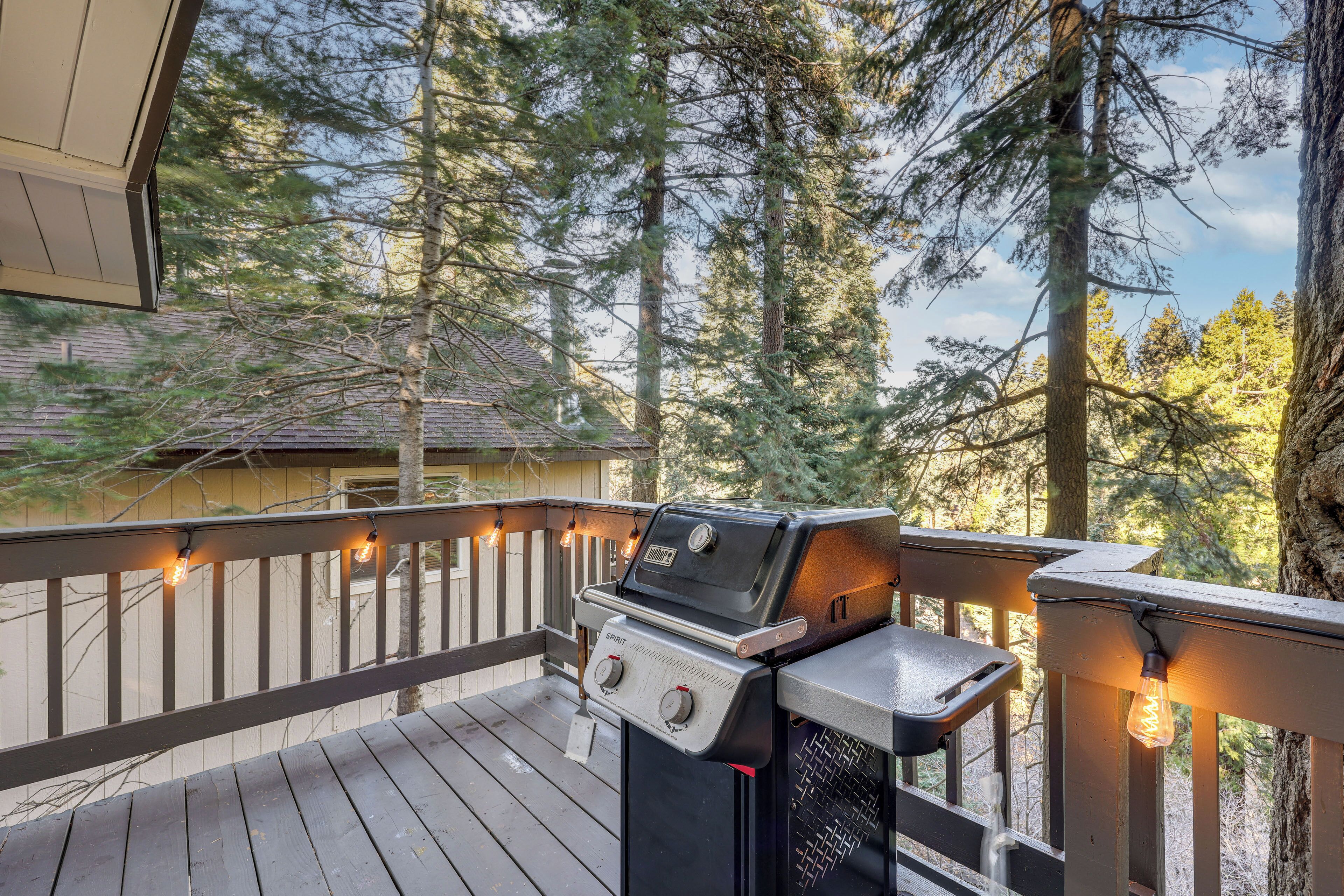A deck with a grill and string lights, surrounded by tall trees.
