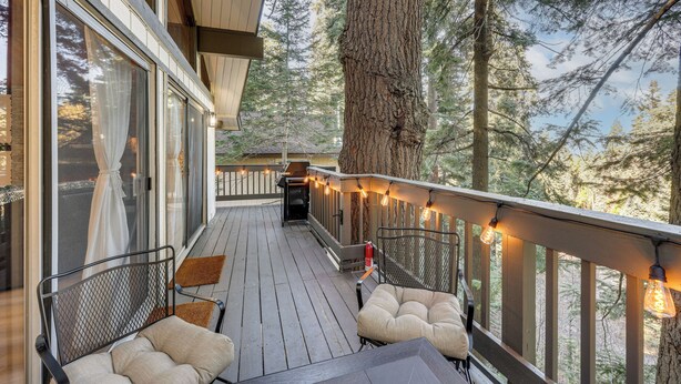 A wooden deck with outdoor seating, string lights, and a view of a forest. - Modern Lake Arrowhead Retreat: 3 Mi to Village (Lake Arrowhead)