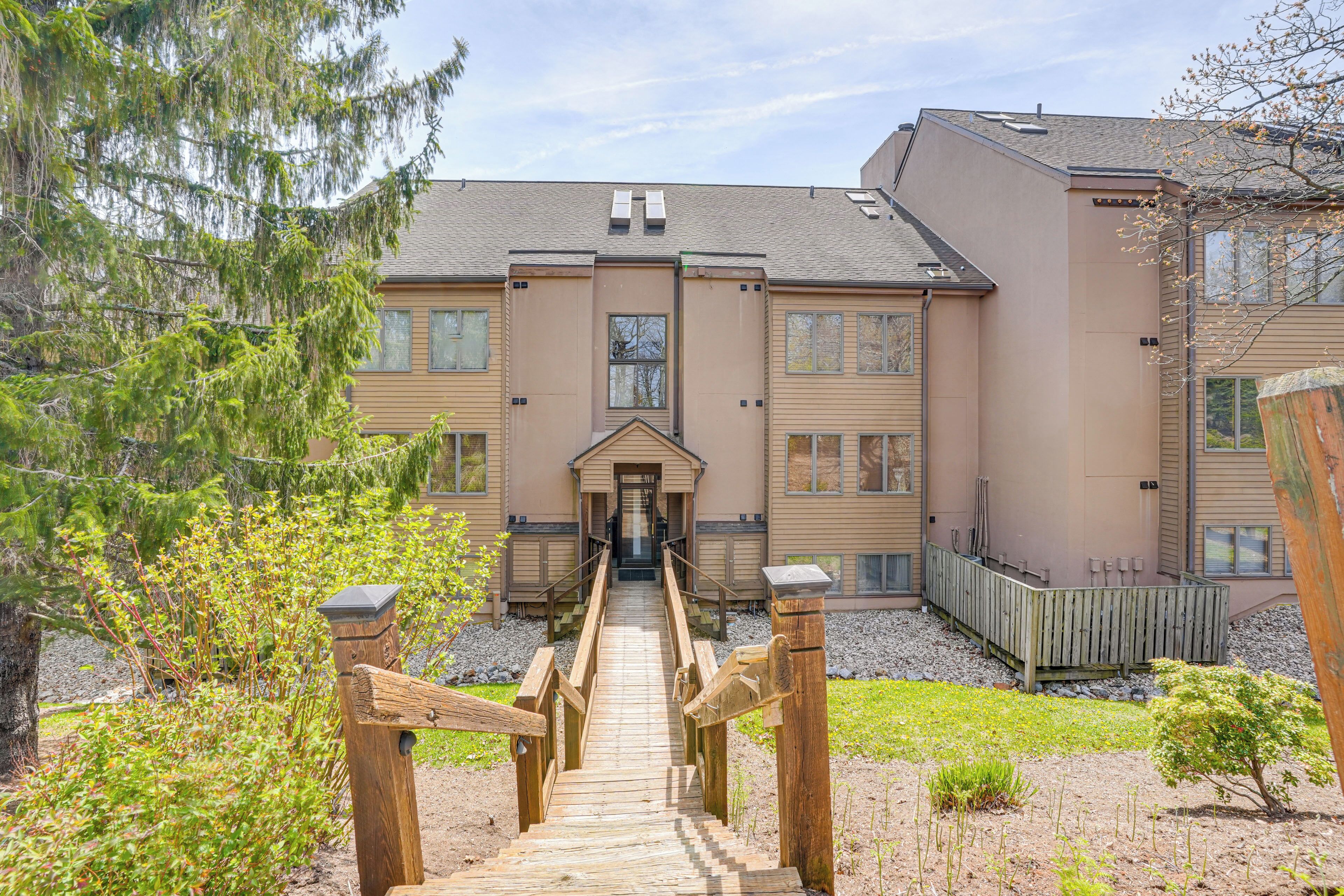 Ein Gebäude mit einem zentralen Eingang, einem hölzernen Weg, der dorthin führt, und einem eingezäunten Gartenbereich.