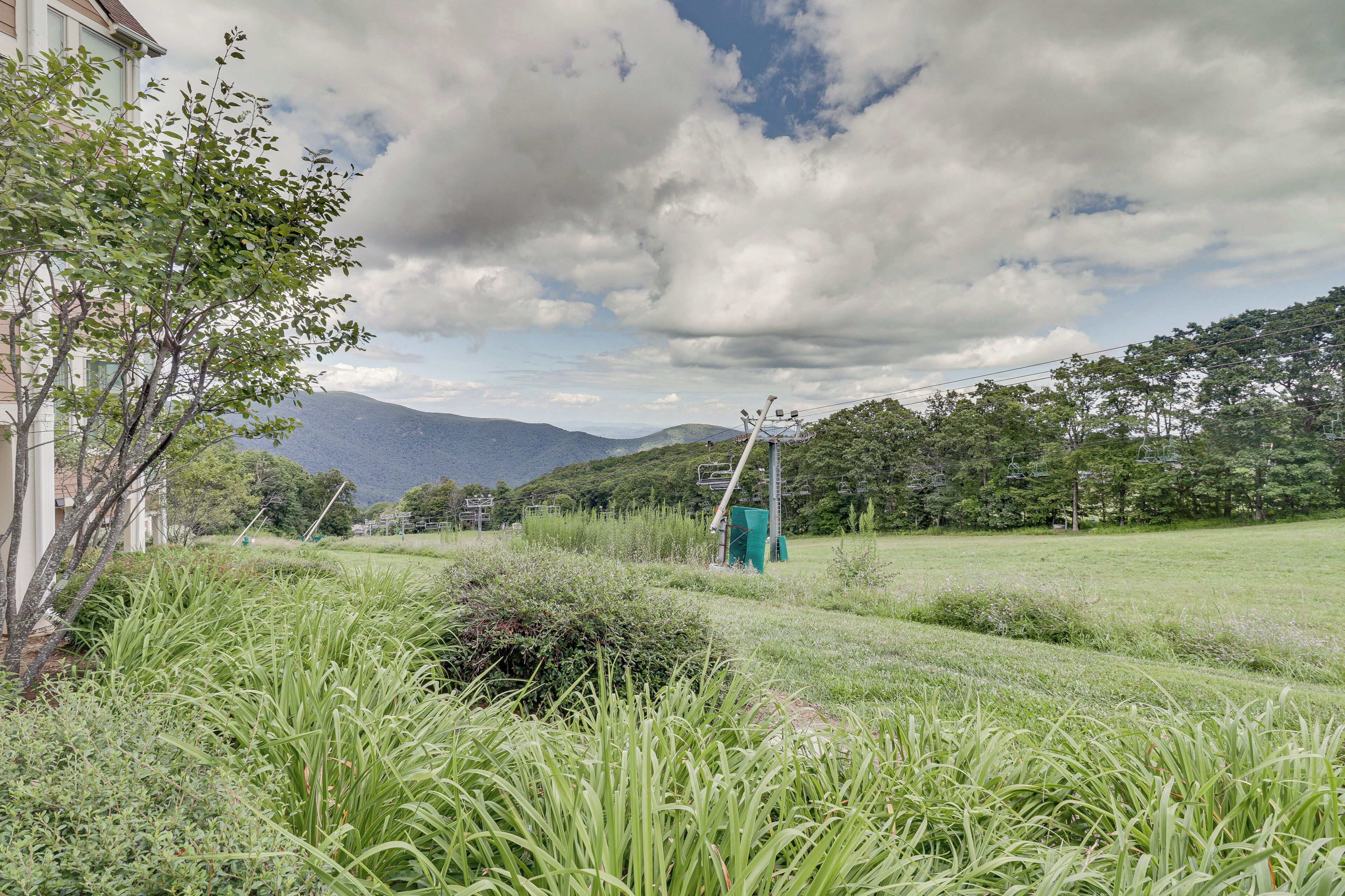 A grassy field with a building on the left and mountains in the background.