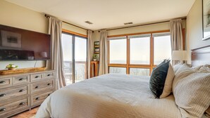A bedroom with a large bed, a dresser, a flat-screen TV, and a balcony with curtains. - Pool Access: Scenic Condo in Wintergreen Resort! (Nellysford)