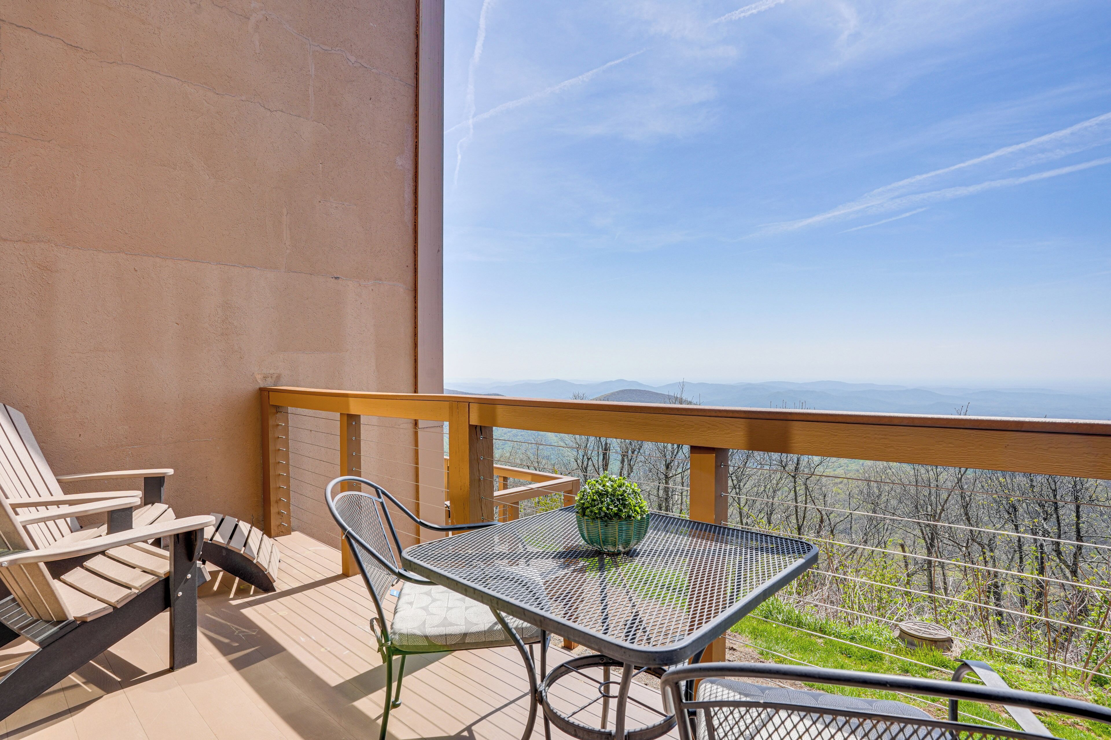 A balcony with a table and chairs, a potted plant, and a view of the mountains.