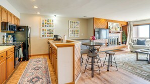 A modern kitchen with wooden cabinets, a central island, and a dining area with stools. - Pool Access: Scenic Condo in Wintergreen Resort! (Nellysford)