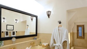 A bathroom with a large mirror, a sink with gold faucets, a robe hanging on the wall, and a bathtub. - Charming Mini Riad 2 Bedrooms Shared Pool (Marrakech)