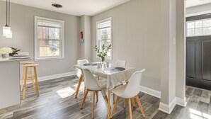A dining area with a table set for four, surrounded by white chairs, a bar area with stools, and a view of the outside through large windows. - 4 Mi to Universities: Quaint Parkville Apartment! (Parkville)