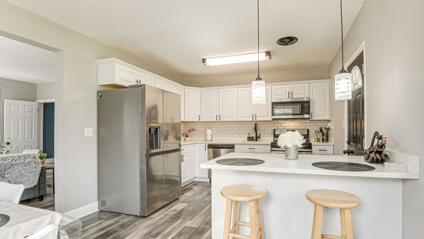 A modern kitchen with white cabinets, stainless steel appliances, and a central island with stools. - 4 Mi to Universities: Quaint Parkville Apartment! (Parkville)