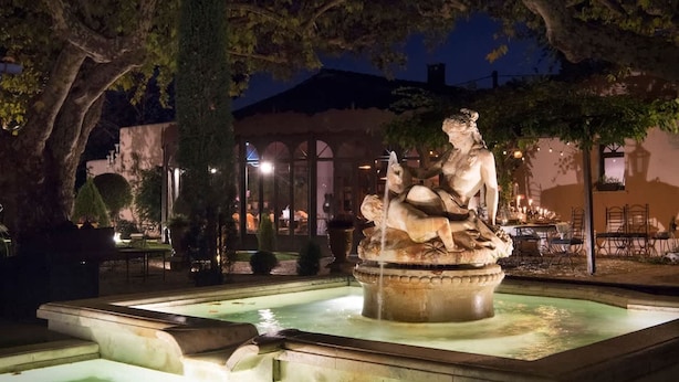 A nighttime outdoor fountain with a statue, surrounded by trees and a building with outdoor seating. - Proven ale House With Pool and spa (Noves)