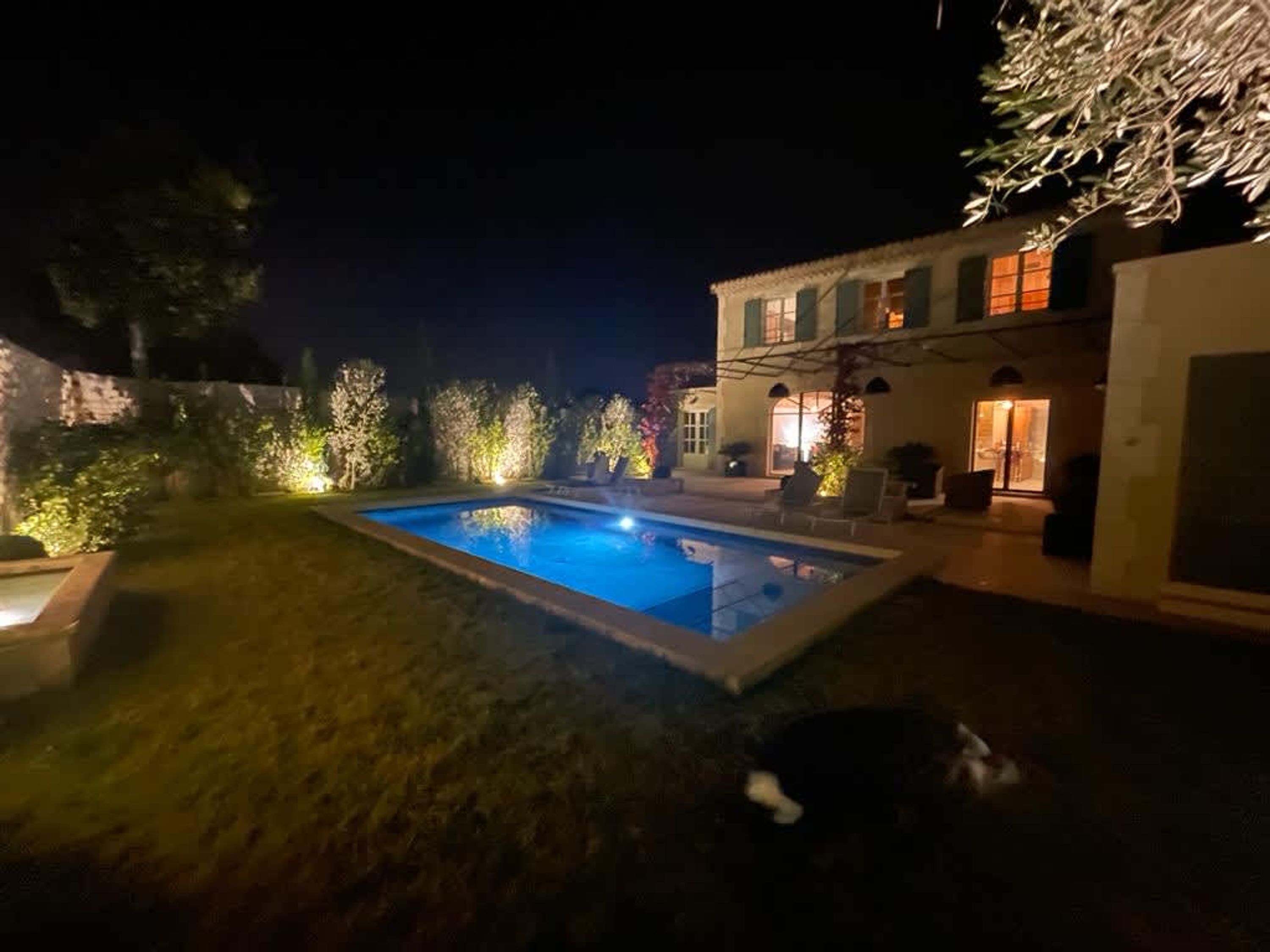 A swimming pool surrounded by a well-lit garden and a building with a balcony.