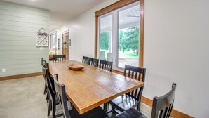 A dining room with a wooden table and chairs, large windows, and a view of greenery outside. - Great for Groups: Family Creekside Home in Loretto (Loretto)