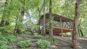 A rustic wooden cabin with a wooden deck, surrounded by dense forest and trees. - Great for Groups: Family Creekside Home in Loretto (Loretto)