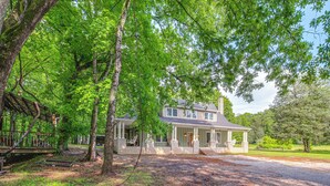 A two-story house with a porch, surrounded by trees and a well-maintained lawn. - Great for Groups: Family Creekside Home in Loretto (Loretto)