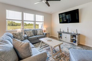 A living room with a sectional sofa, a coffee table, a TV mounted on the wall, and a window with blinds. - Modern Millville Home: 5 Mi to Beach & Boardwalk! (Frankford)