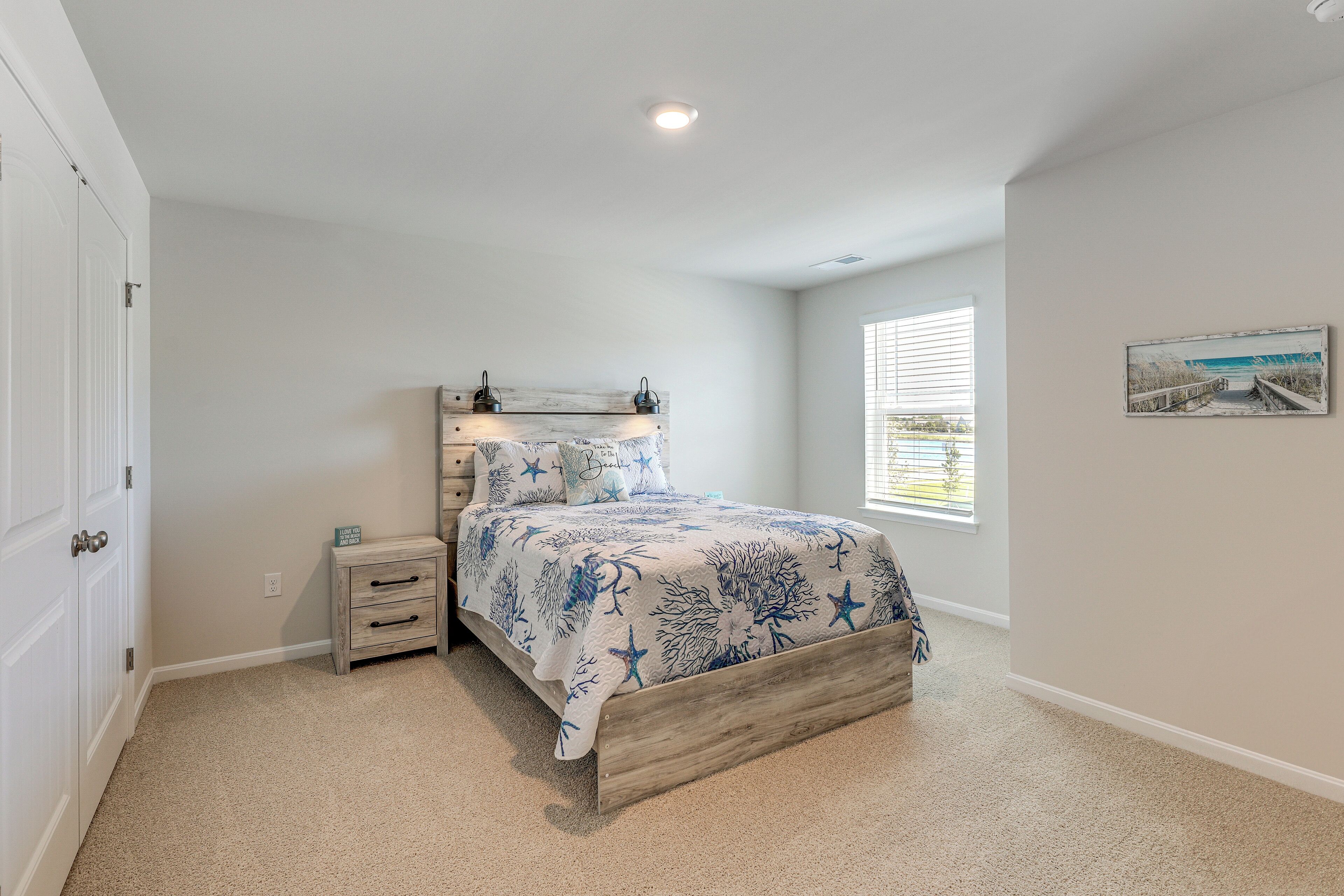 A bedroom with a bed, a nightstand, a window, and a door.