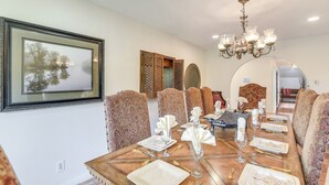 A dining room with a long table set for a meal, patterned chairs, a chandelier, and a framed picture on the wall. - 2 Mi to Dtwn: Spacious Angleton Home w/ Courtyard! (Angleton)