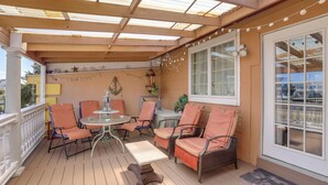 Een overdekt terras met houten vloer, een tafel met stoelen en een raam met gordijnen.