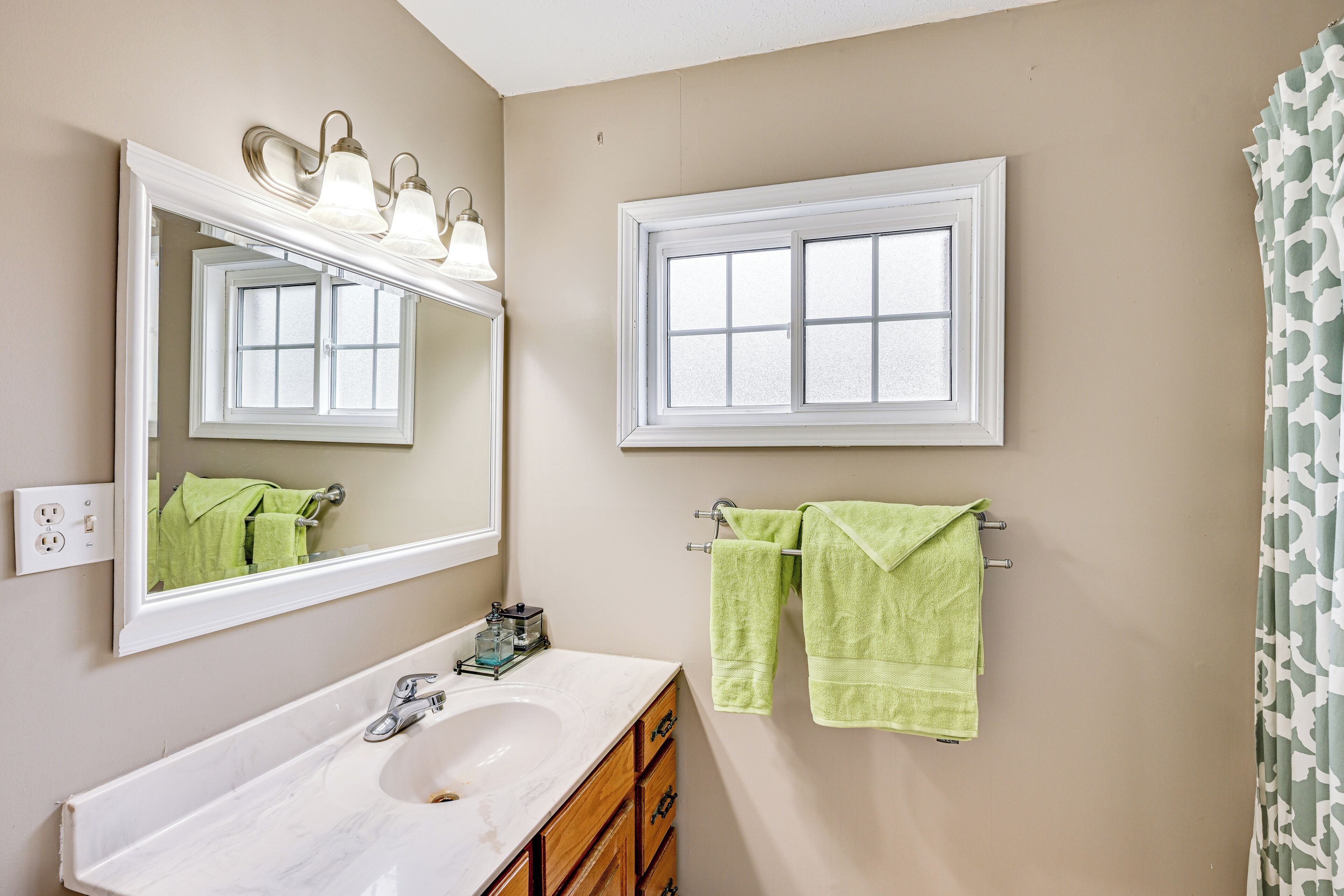 A bathroom with a white sink, a mirror, a window, and two towels hanging on a towel rack.