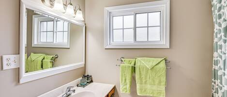 A bathroom with a white sink, a mirror, a window, and two towels hanging on a towel rack.