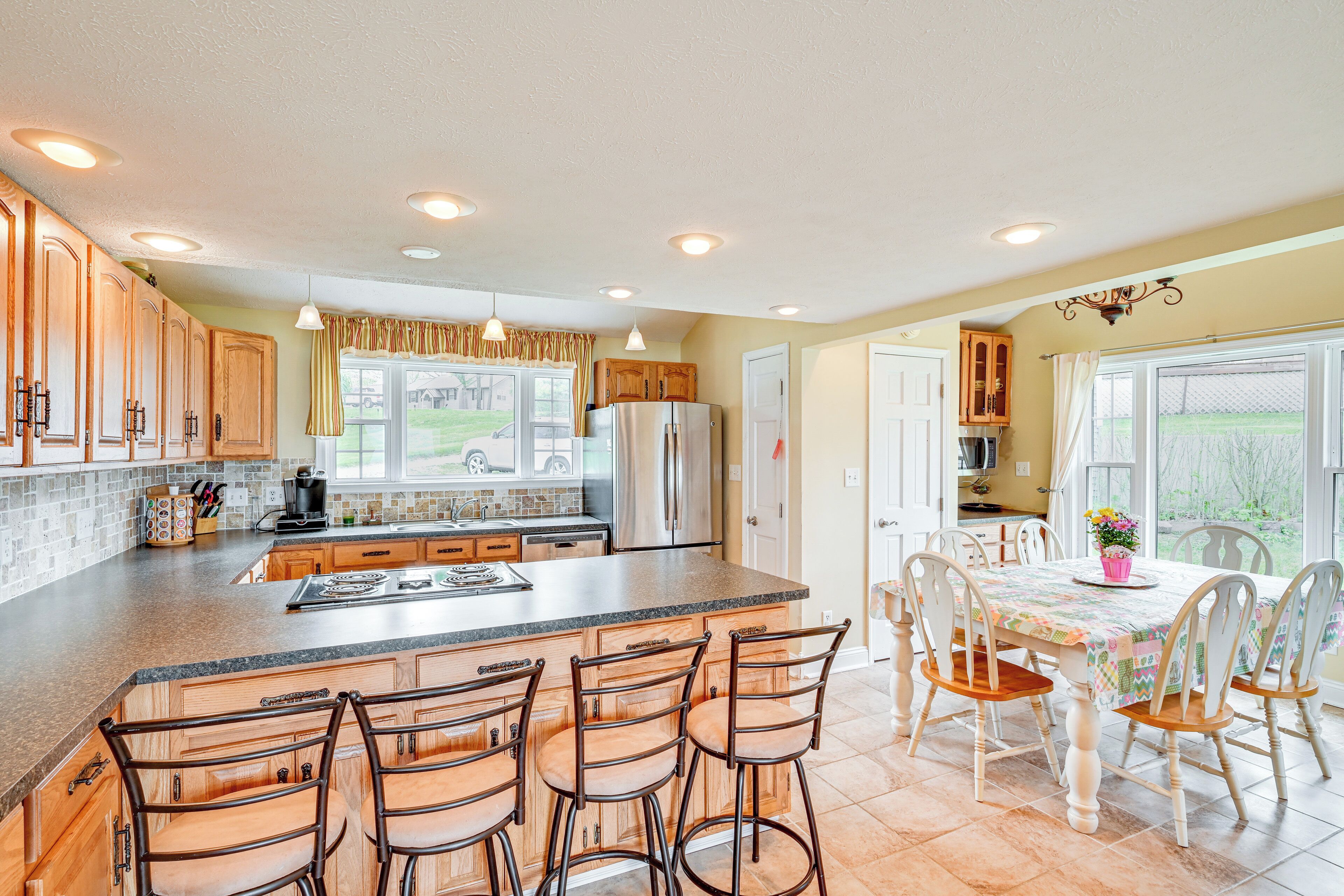 A kitchen with a central island, bar stools, and a dining table with chairs.