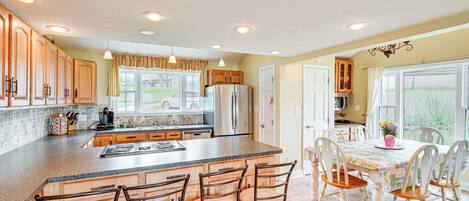 A kitchen with a central island, bar stools, and a dining table with chairs.