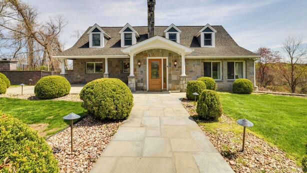 A two-story house with a stone facade, a central entrance with a wooden door, and a stone chimney. There are two small windows on the upper floor and a covered porch with columns. - Outdoor Entertainment Areas: Spacious Katonah Gem! (Katonah)